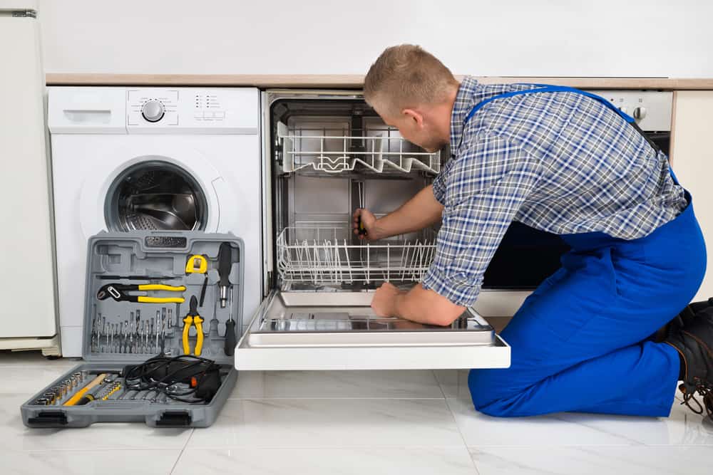 Young Man In Overall With Toolbox Repairing Dishwasher